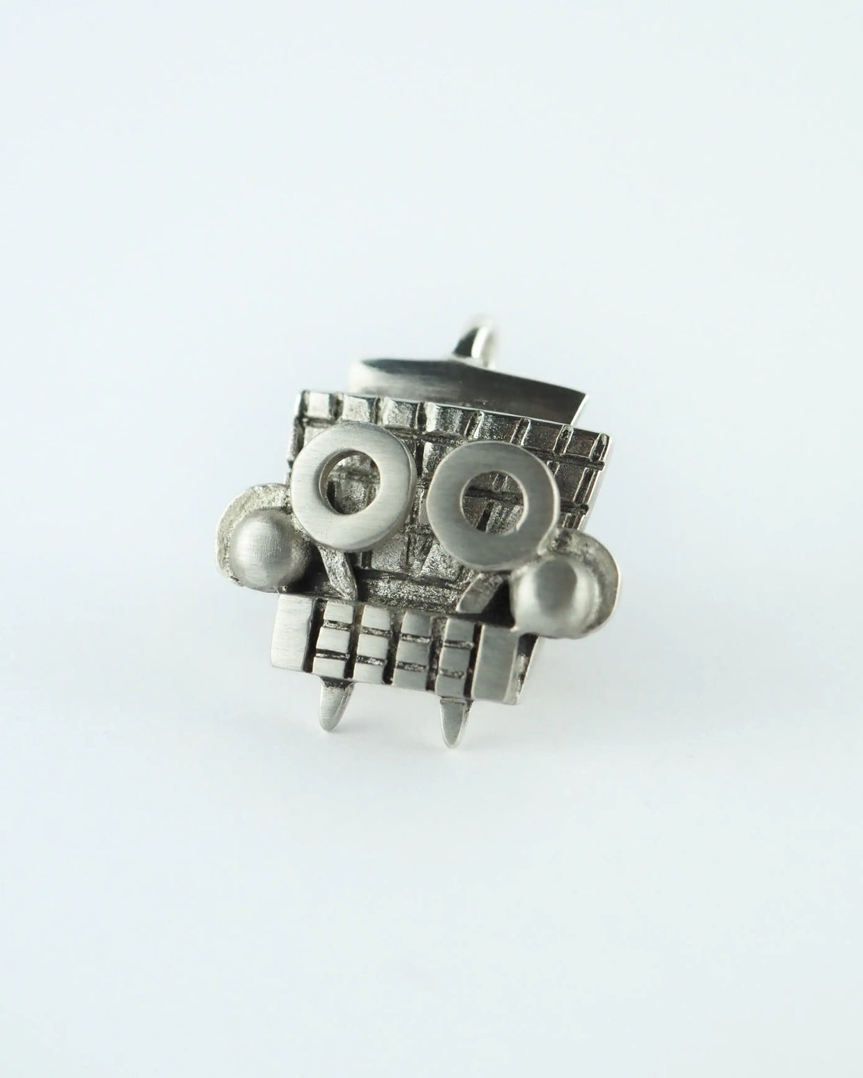 Colgante plateado de metal con figura tipo tótem y detalles enrejados