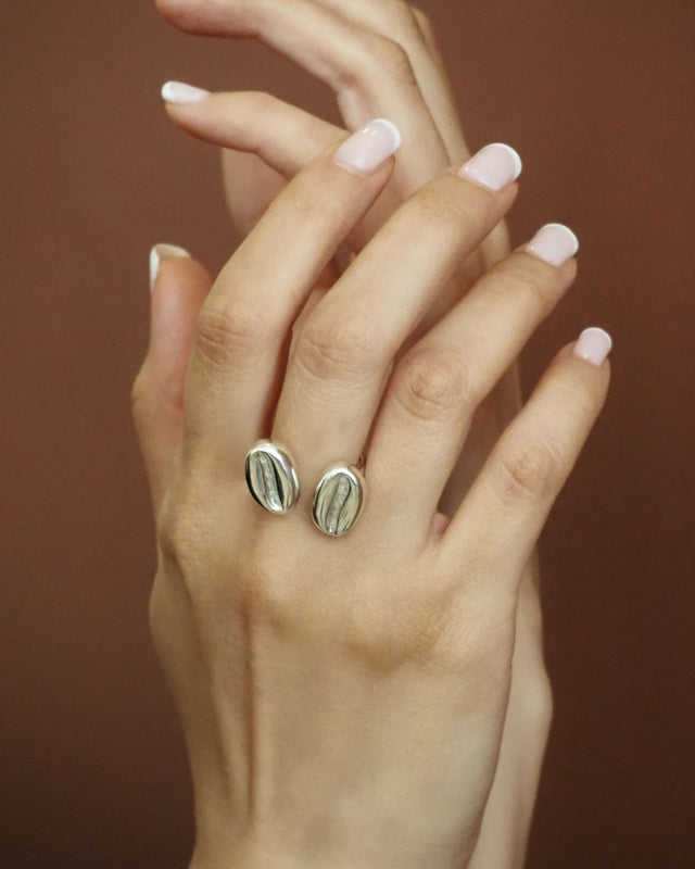 Par de anillos ovalados plateados con inserto oscuro sobre la mano