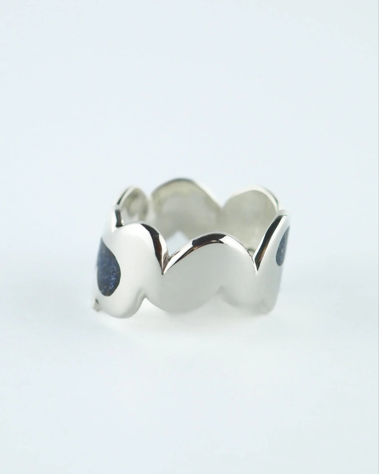 Anillo ancho plateado con piedras azules oscuras y bordes ondulados