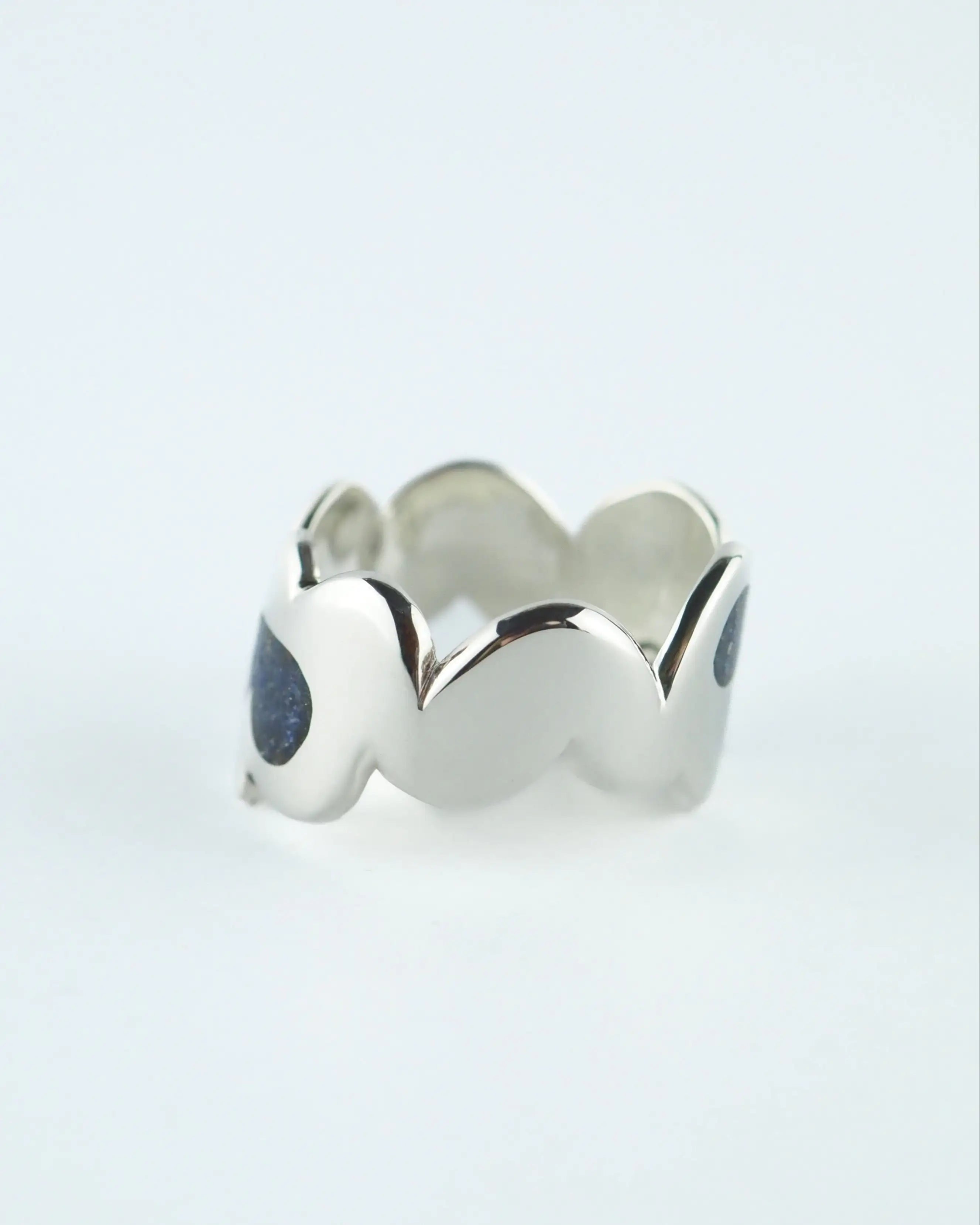 Anillo ancho plateado con piedras azules oscuras y bordes ondulados