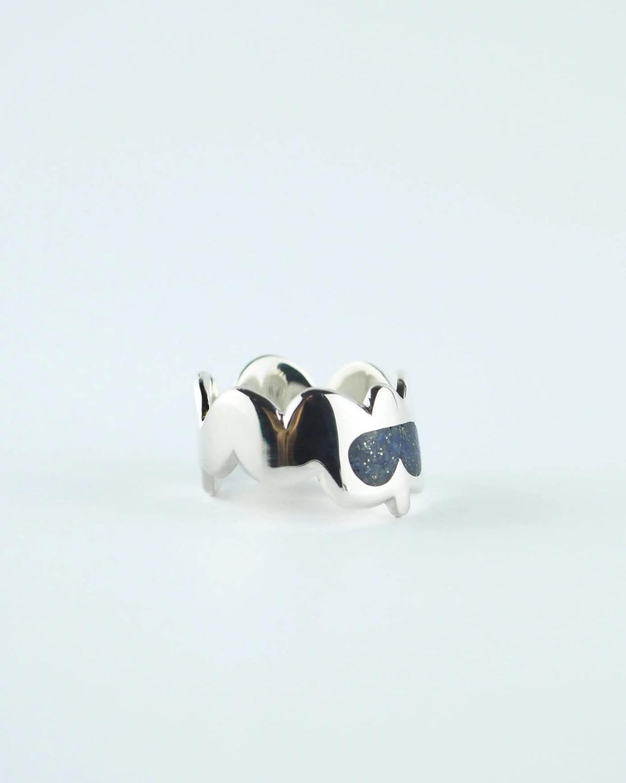 Anillo plateado con piedras azules en forma de gota sobre banda ondulada