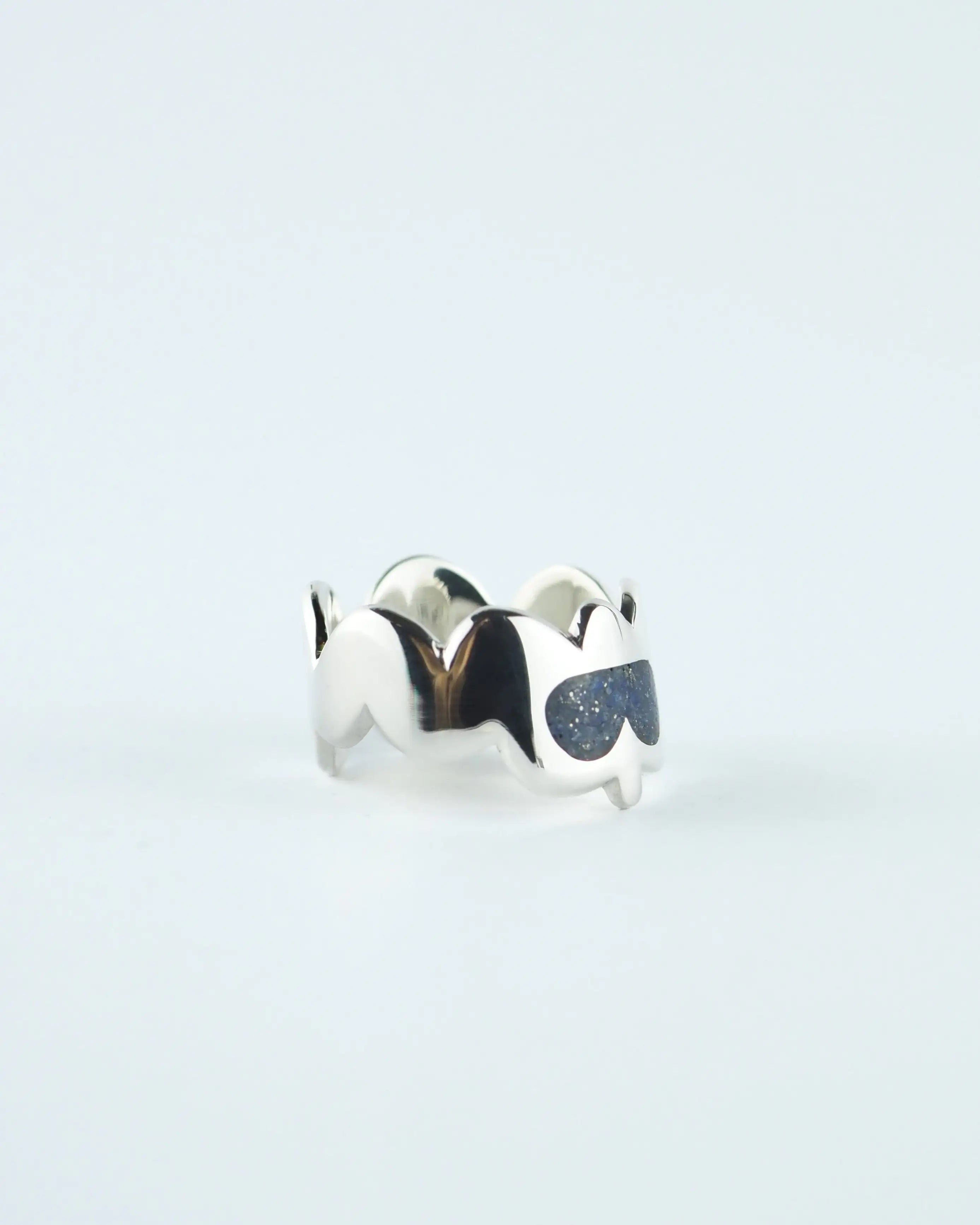 Anillo plateado con piedras azules en forma de gota sobre banda ondulada
