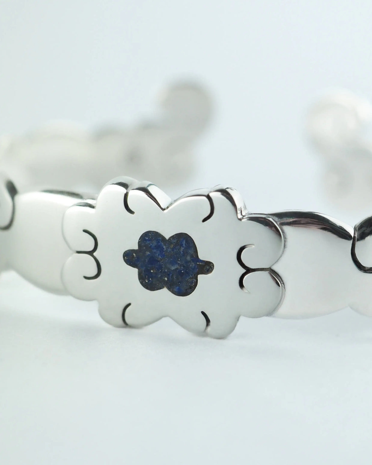 Pulsera plateada con flor azul central y decoración calada en los eslabones.
