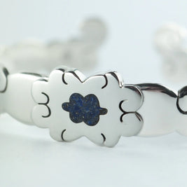 Pulsera plateada con flor azul central y decoración calada en los eslabones.