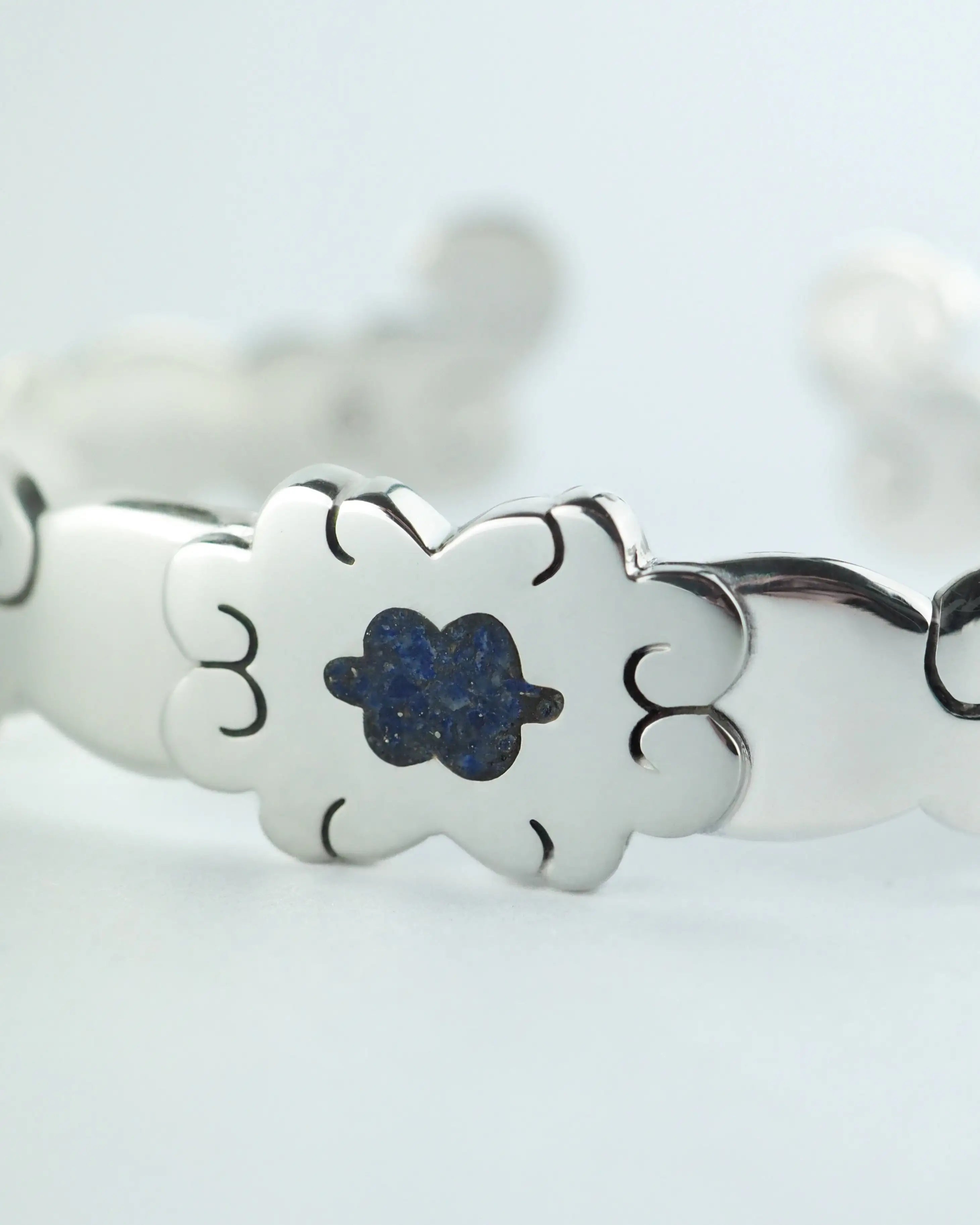 Pulsera plateada con flor azul central y decoración calada en los eslabones.