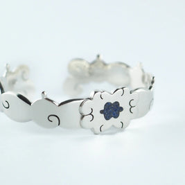 Pulsera plateada con flor azul central y cierre metálico, diseño calado.