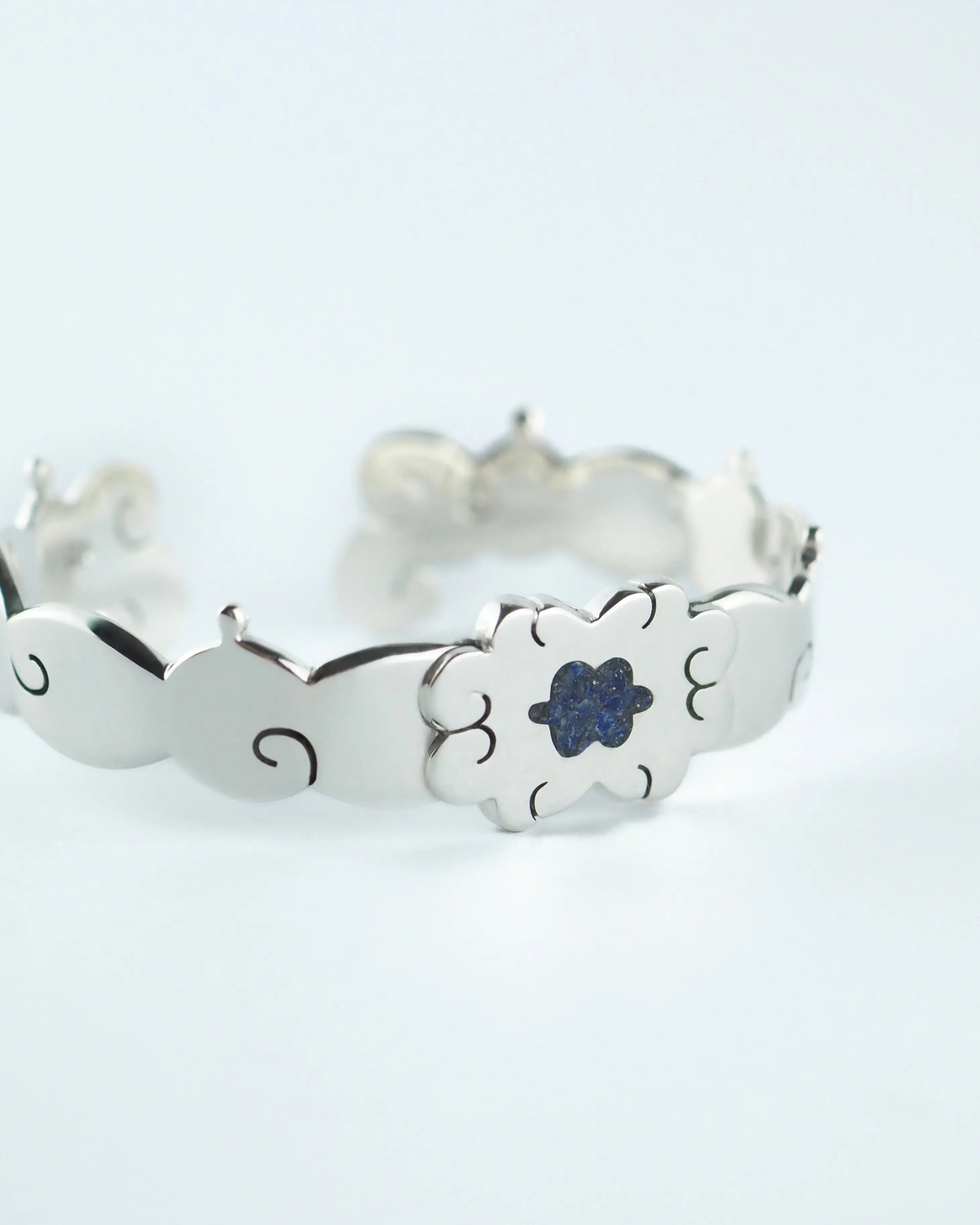 Pulsera plateada con flor azul central y cierre metálico, diseño calado.