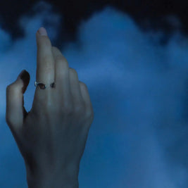 Anillo Timilin plateado en el dedo, con ranuras y detalles negros curvos.